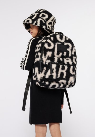 Zwarte en crèmekleurige nepbont rugzak en emmerhoed met gedurfde letterpatronen, voorzien van een voorrits en verstelbare zwarte banden.