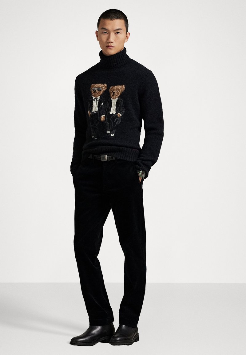 Pull à col roulé noir avec un design brodé de deux ours en smoking. Associé à un pantalon en velours côtelé noir et des bottes noires brillantes.