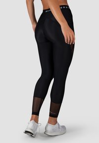 Zwarte leggings met een hoge tailleband, voorzien van mesh-panelen op de onderbenen. Glad textuur en aansluitend ontwerp, gecombineerd met witte sportschoenen.