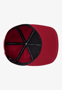 Cappellino da baseball rosso con visiera piatta, dotato di una fodera interna nera e dettaglio di marchio all'interno. Il tessuto ha una texture liscia.