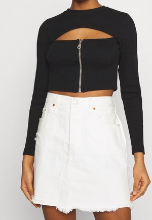 Schwarzes, geripptes Langarm-Crop-Top mit einem Ausschnitt vorne und einem silbernen Reißverschluss. Kombiniert mit einem weißen Jeansrock mit ausgefranstem Saum und Taschen.