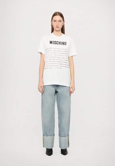 T-shirt en coton blanc avec le logo "MOSCHINO" noir, présentant un design de texte imprimé. Associé à un jean large en denim bleu clair et des bottines noires.