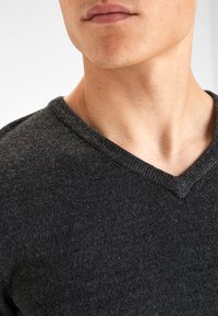 Suéter de punto en color gris oscuro con escote en forma de V, hecho de una tela suave y texturizada. Presenta un cuello acanalado y un ajuste ceñido en el cuello y los hombros.