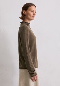Brązowy sweter z długim rękawem w stylu golfu, wykonany z miękkiego materiału. Charakteryzuje się dopasowanym krojem i ściągaczami przy rękawach. Prosty styl, neutralny odcień.
