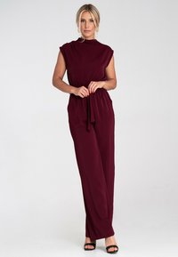 Burgundowy kombinezon z krótkimi rękawami, dopasowany w talii i z szerokimi nogawkami, wykonany z gładkiego materiału. Cechuje się minimalistycznym designem i brakiem widocznych zapięć.
