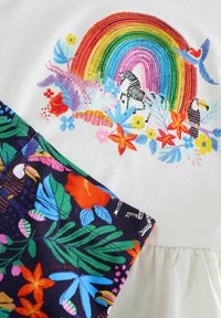 Puuvillamekko, jossa on värikäs sateenkaari ja kukkakuviointia. Tumma kangas, jossa on trooppisten lehtien ja tukaanin kuvio alahelmassa.