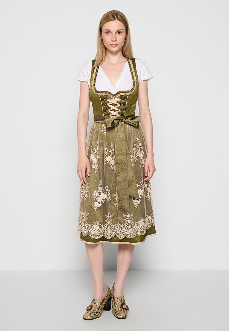 Traditionelles grünes Dirndl mit tailliertem Oberteil, Schnürung vorne, floralem Stickerei und einem halbtransparenten Überwurf. Getragen mit einer weißen Bluse.