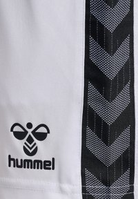 Weiße Sportshorts mit einem schwarzen Hummel-Logo und einem strukturierten schwarz-weißen Chevron-Muster entlang der Seitennähte.