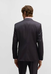 Donkergrijze colbert met gelapte revers, knoopmanchetten en een gladde textuur. Heeft een getailleerde pasvorm met een vent in de rug.