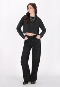 Felpa nera corta con maniche lunghe e una leggera texture, abbinata a jeans neri a vita alta e a gamba larga. Distintivo collana a catena a più strati.