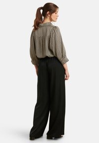 Blouse met een zigzagpatroon in zwart en crèmekleur, met puffed mouwen en een geplooide achterkant, gecombineerd met vloeiende zwarte wijde broekspijpen.