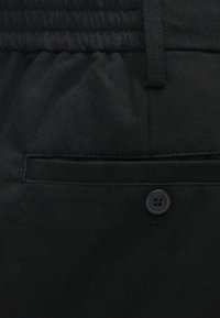 Čierna tkanina s textúrovaným povrchom obsahujúca elastický pás, zapínanie na tlačidlo a ploché vrecko.