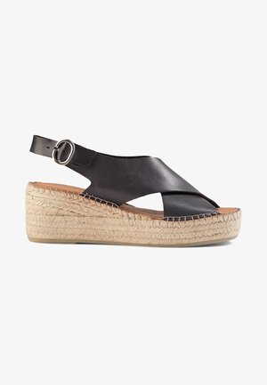 Black leather wedge sandals with a crossover design, jute rope sole, adjustable ankle strap, and smooth texture.