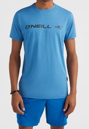 Mann, der ein hellblaues O'Neill T-Shirt und leuchtend blaue Shorts mit einem schwarzen Armband am linken Handgelenk trägt.