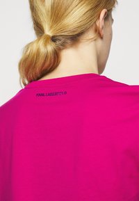 Camiseta de algodón color magenta con cuello redondo y mangas cortas. Presenta "KARL LAGERFELD" bordado en negro en la parte posterior del cuello.