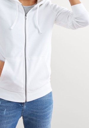 Witte hoodie met ritssluiting en trekkoorden, gemaakt van textuurstof, met twee frontzakken, gedragen met blauwe spijkerbroek.