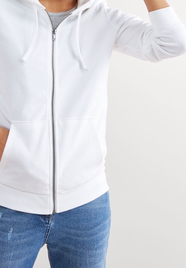 Felpa bianca con zip e cordini, realizzata in tessuto strutturato, con due tasche frontali, indossata con jeans blu.