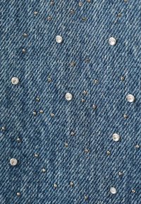 Tejido de mezclilla con un tono azul, que presenta brillantes tachuelas plateadas y metálicas esparcidas, creando un diseño texturizado en toda la superficie.