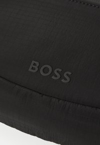 Giubbotto nero in stile piumino con texture a rombi e logo "BOSS" in rilievo. Superficie liscia con un design elegante e accenti minimali.