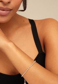 Bracelet en argent avec des perles lisses et arrondies, porté sur un poignet nu, contrastant avec un haut noir et un teint de peau chaud.