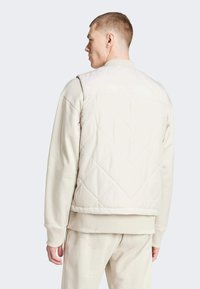 Chaqueta de crema acolchada con cuello redondo, mangas largas y puños acanalados, que presenta una textura suave y un patrón de costura diagonal.