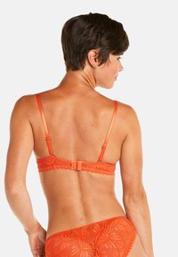 Soutien-gorge en dentelle orange avec bretelles ajustables, présentant des bords festonnés et une fermeture à crochet. La vue arrière met en valeur un motif complexe et une texture douce.