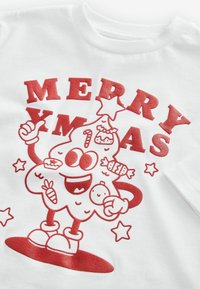 Weißes Kurzarmhemd mit rotem Grafikdesign eines lächelnden Charakters, der weihnachtliche Elemente, "MERRY XMAS" und Sterne enthält.