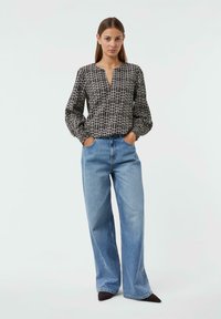 Schwarz-weiße karierte Bluse mit langen Ärmeln, V-Ausschnitt und gerafften Bündchen, kombiniert mit hellblauen weiten Jeans und dunklen spitzen Schuhen.