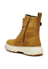Stivale alla caviglia in suede marrone con suola bianca, dotato di zip laterale, stringhe frontali, colletto imbottito e dettaglio del logo in rilievo.