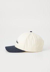 Baseball cap with a cream crown and dark navy visor. Features embroidered black script. Made of fabric with a textured brim.