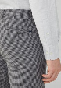 Pantaloni con motivo pied de poule grigio e nero, chiusura con bottoni, dettaglio tasca e piccola etichetta del marchio vicino alla tasca laterale.