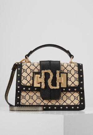 Sac à main à motif beige et noir avec des clous dorés, grande fermeture décorative dorée, poignée supérieure et bandoulière amovible sur surface blanche.