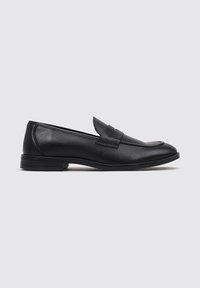 Mocasines de cuero negro con un acabado suave, punta redondeada, correa decorativa y una suela de goma texturizada y baja. Diseño simple y clásico.
