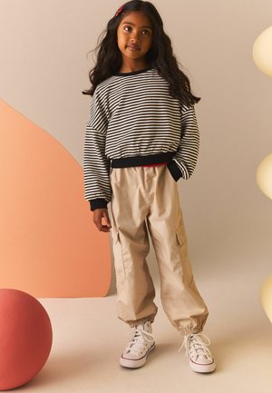 Gestreifter schwarz-weißer Pullover mit elastischem Saum, beiges Cargo-Hose mit elastischen Bündchen, weiße High-Top-Sneaker, roter Haarklammer.