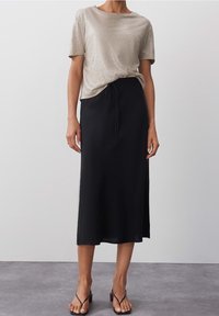 Lyhyt hiha, metallinhohtoinen vaaleankultainen toppi, joka on yhdistetty pitkä musta hame, jossa on joustava vyötärö ja naru. Asusteena mustat sandaalit.