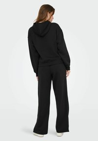 Completo felpa nera in tessuto morbido. Caratterizzato da cappuccio, maniche lunghe e pantaloni larghi con cintura elastica. Design semplice e minimal.