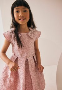 Roosa kleit tekstuurse kangaga, millel on peen muster, kapuutsiga varrukad ja õladel paeladetailid. Plisseeritud seelikudisain.