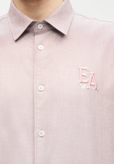 Ροζ ανοιχτό πουκάμισο με γιακά, με κεντημένα γράμματα "EA" στο αριστερό μέρος του στήθους.