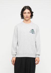 Sudadera gris con mangas largas, cuello redondo y un gráfico verde en el pecho. Tiene una textura suave y puños acanalados.
