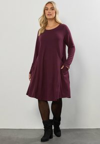 Bordowa sukienka z długim rękawem i okrągłym dekoltem, z bocznymi kieszeniami i rozszerzaną sylwetką, wykonana z miękkiej, teksturowanej tkaniny.