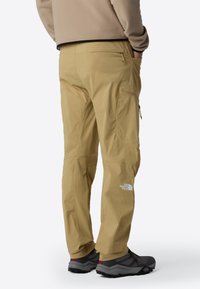 Beige outdoor pants with a relaxed fit, featuring side pockets and a logo detail. Made from lightweight, durable fabric.