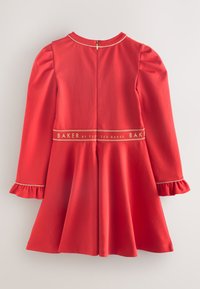 Rød kjole med langeærmer, flæsekantede manchetter og en udvidet nederdel. Har en bånd med gulddetaljer med teksten "BAKER by Ted Baker".