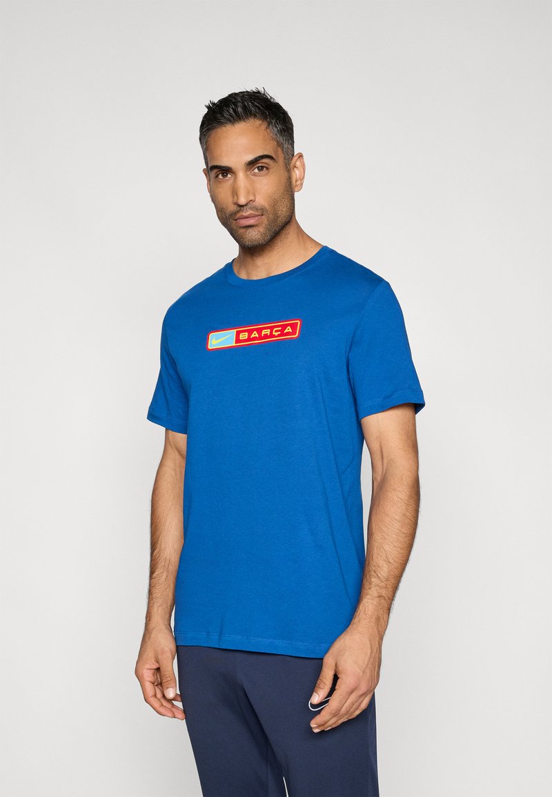 Μπλε βαμβακερό μπλουζάκι με στρογγυλή λαιμόκοψη και κοντά μανίκια, με ορθογώνιο κόκκινο και κίτρινο γραφικό ετικέτα που γράφει "BARÇA."