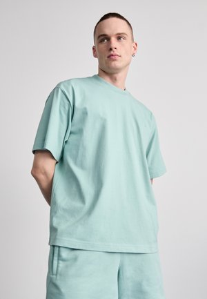 T-shirt vert menthe à manches courtes en coton doux. Coupe décontractée avec col rond et détail de logo subtil sur la poitrine. Pièce assortie en bas.