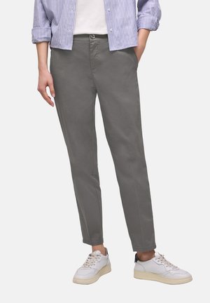 Person iført grå, tilspidsede bukser, hvide sneakers, hvid skjorte og blåstribet skjorte med knapper, ærmerne rullet op.