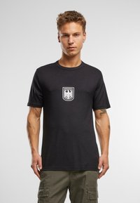 Fekete pamut póló, középen fehér pajzs logóval, rajta a "BUNDESWEHR" felirattal. Normál gallérú, rövid ujjú, sima textúrájú.