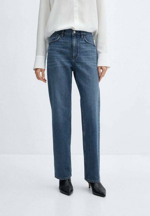 Jeans in denim blu a gamba dritta con vita alta, cuciture accentuate e tasche frontali, abbinati a una camicia bianca con bottoni e tacchi neri.