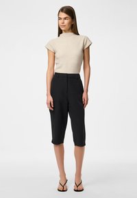 Beige knit top with short sleeves, high neck; black cropped trousers with a tailored fit; model wearing black flip-flops.