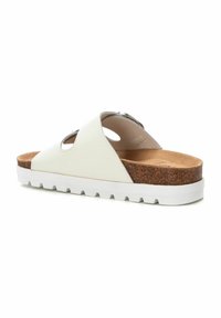 Sandalia plana blanca que presenta una parte superior de dos piezas con detalles recortados, una plantilla de corcho y una suela de goma blanca texturizada.