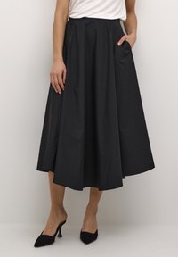 Svart midikjol, tillverkad av lättviktig tyg, med hög midja, voluminös silhuett och sidofickor. Matchas med svarta klackar.